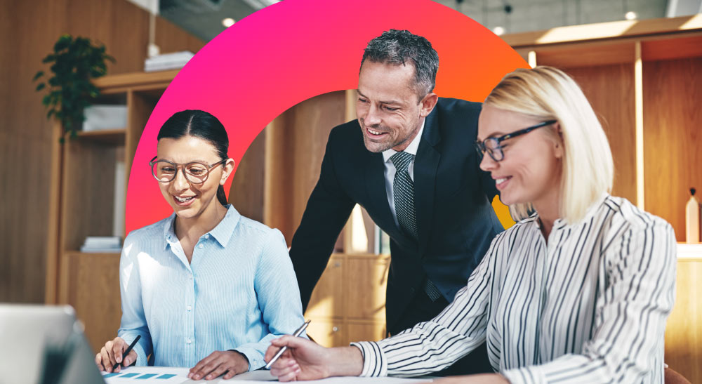 Three employees review paperwork over a table