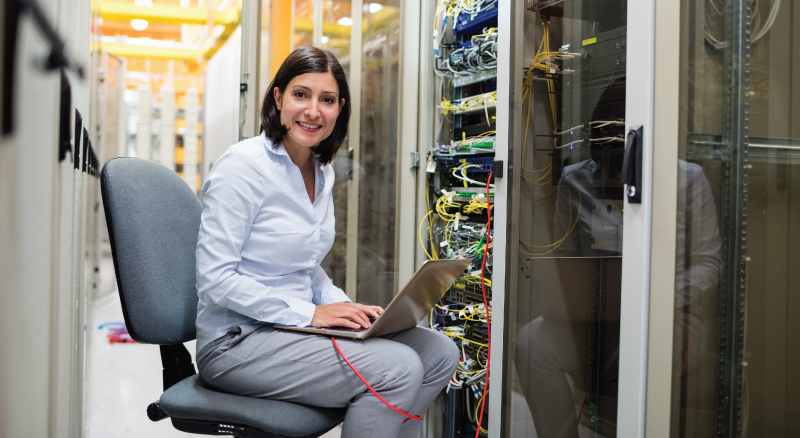 Woman in data center with laptop connected to server