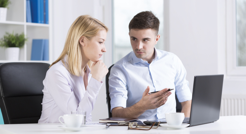 Man explaining something to woman in office by computer