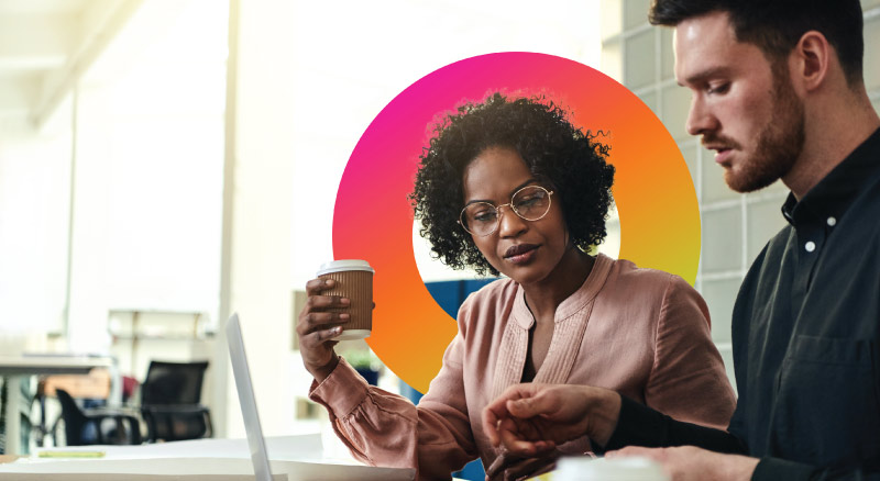 Two co-workers focused on their conversation review documents while one holds a cup of coffee
