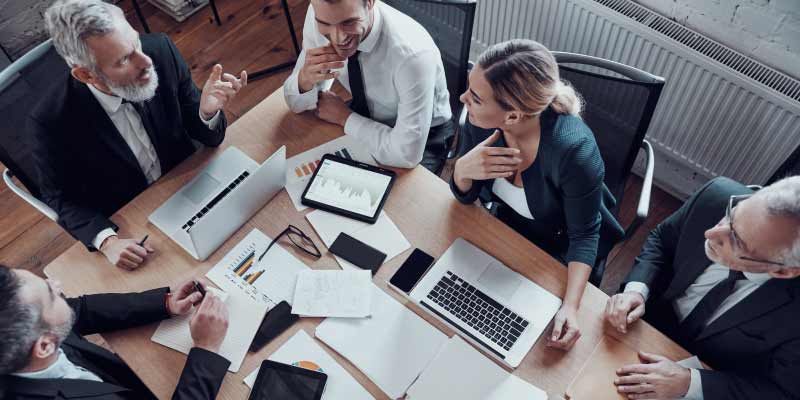 A group of professionals is engaged in a business meeting, working with laptops and documents on a table