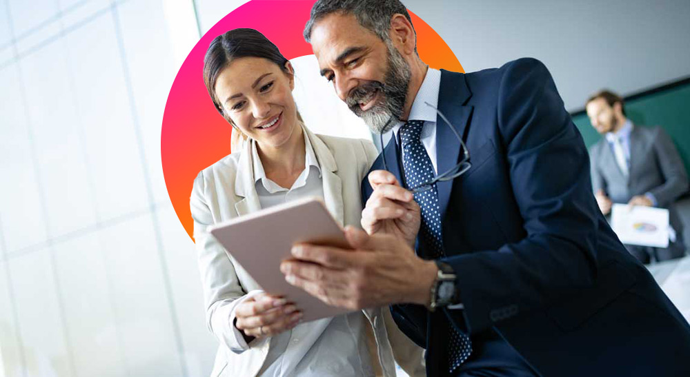 Two people are looking at a tablet, with a third person in the background