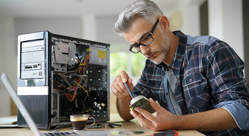 A person is seated at a desk, working on computer hardware components with tools and a laptop nearby