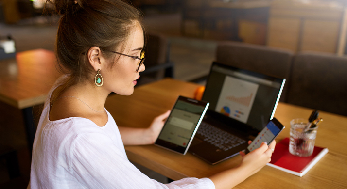 A person is focused on their laptop with a smartphone in a casual indoor setting