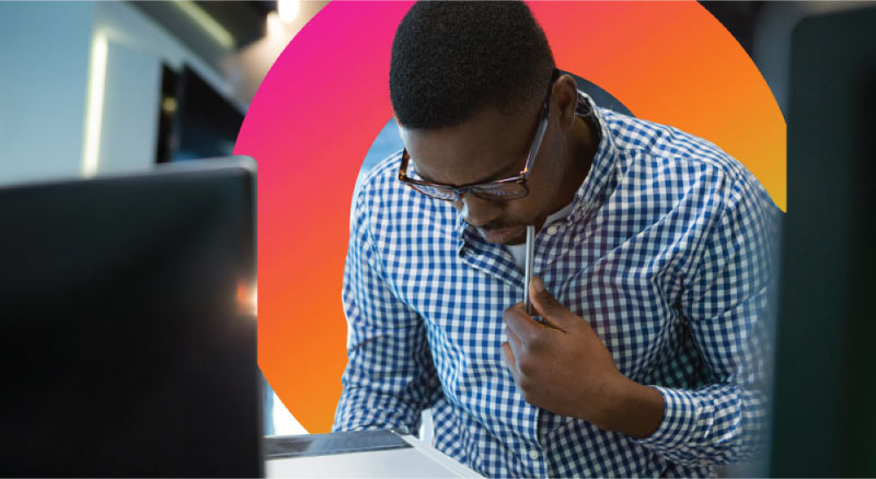 Concentrated man holds pencil looking over laptop