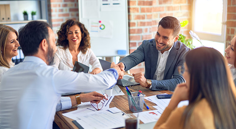 Two individual shaking hands over a table during a business meeting