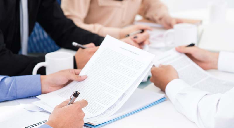 Individuals in a business meeting are examining documents