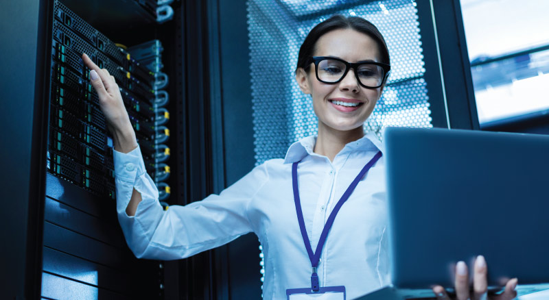 Woman in data center room smiling and holding laptop