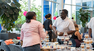 A group of people at an SHI hosted indoor event with a dessert table in the foreground