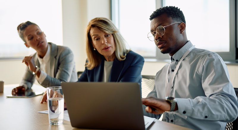 Three people review a laptop during an office meeting