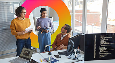 Three people in conversation behind office computer desks