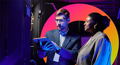 A person reviewing information on a tablet while another examines a server rack