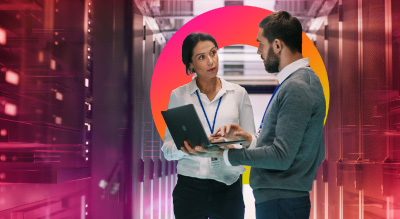 Two people reviewing information on a laptop while standing in a data center