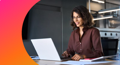 A woman seated at a desk, focused on her laptop, surrounded by a tidy workspace