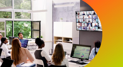 A diverse group of people seated in a conference room, focused on a large screen displaying a presentation