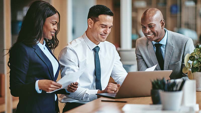 Two males and one female employees discussing documents with laptop open