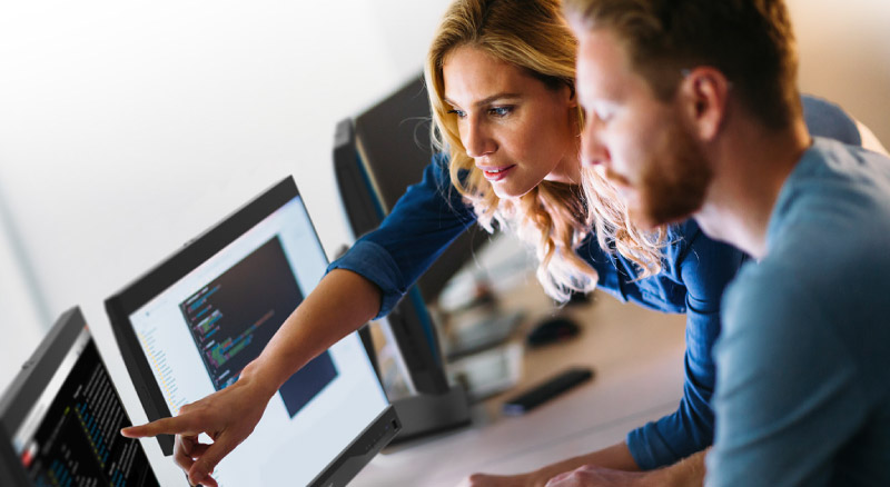 Coworkers looking at two desktop screens