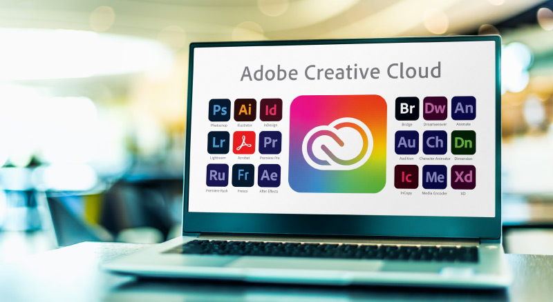 A laptop displaying Adobe Creative Cloud and Adobe suite icons on its screen