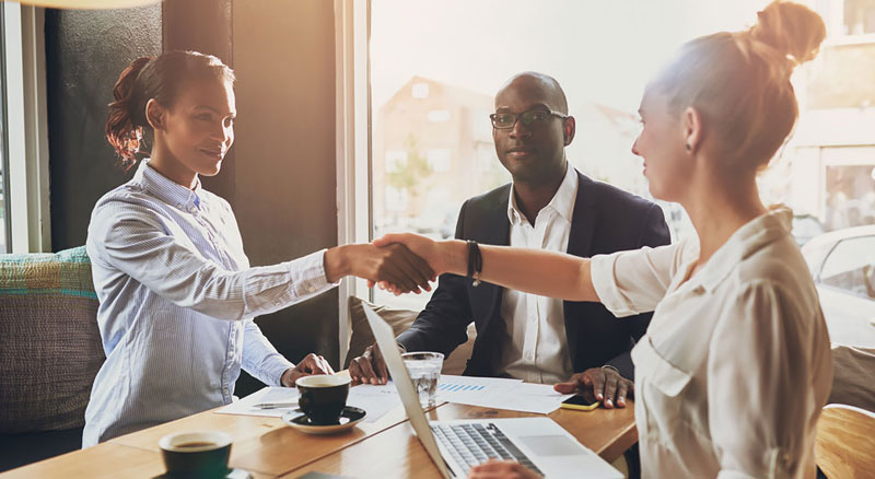 A professional meeting where three individuals are shaking hands to signify partnership