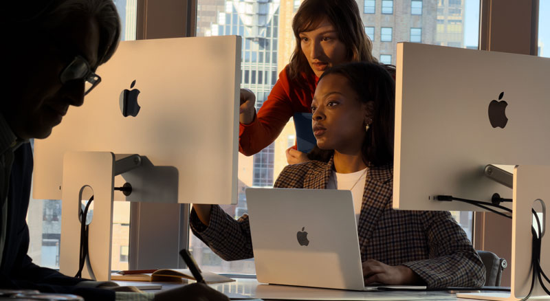 Two employees review information Apple monitor displays