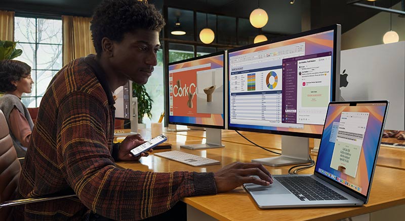 A person holding a closed mac laptop in a modern office filled with plants