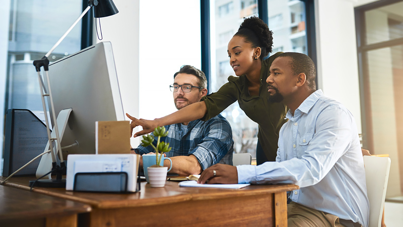 Person points at desktop monitor as two people take a closer look