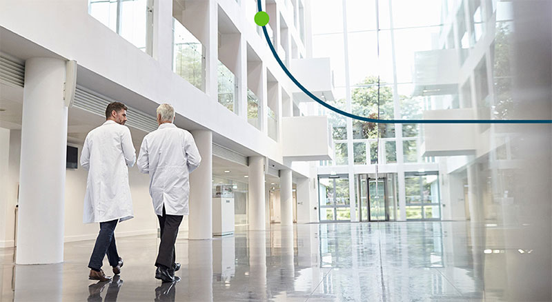 Two individuals in white coats walking through a spacious, modern building with large windows