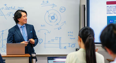 A presenter explaining diagrams and text on a whiteboard to two attendees in a meeting room.