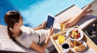 A person relaxing by a pool, reading a book and enjoying breakfast.