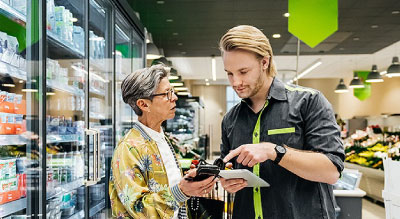 A store employee assisting a customer with a payment device in a grocery store.