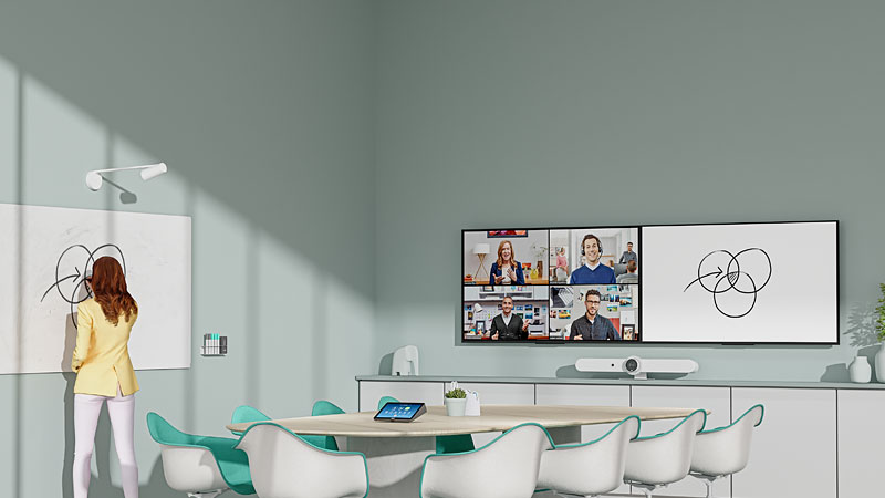 Woman writes on whiteboard which which displays on screen besides a remote video call with four people