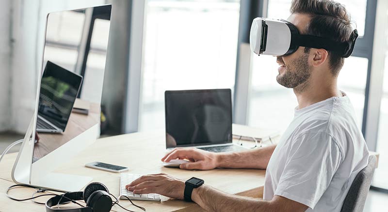 employee using virtual reality headset and computers at desk