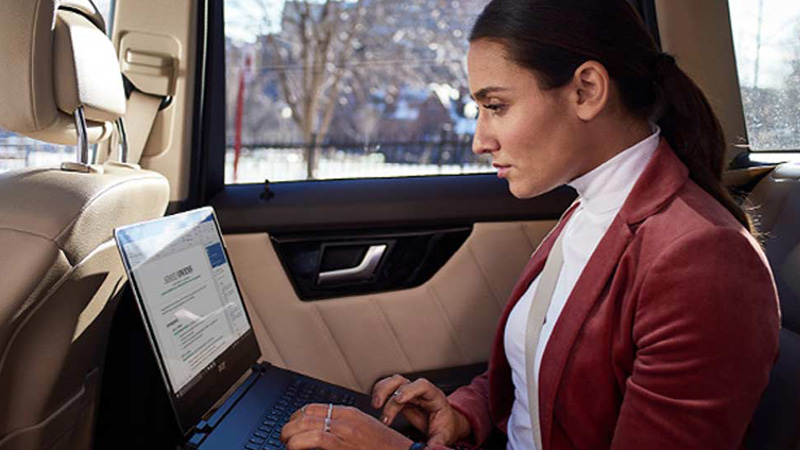 Woman works on laptop in the backseat of a moving car