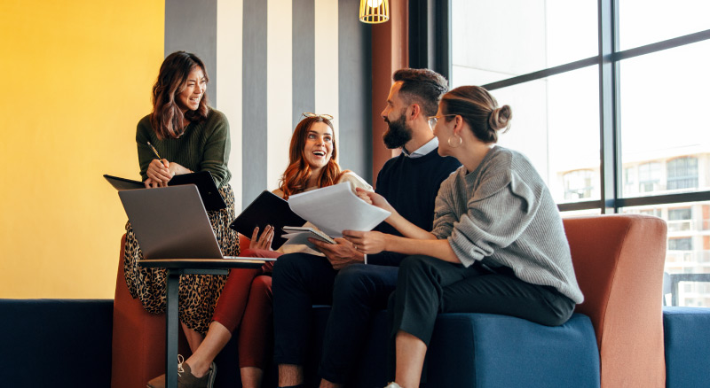 Multicultural businesspeople working in an office lobby. Group of happy businesspeople smiling while sitting together in a co-working space.
