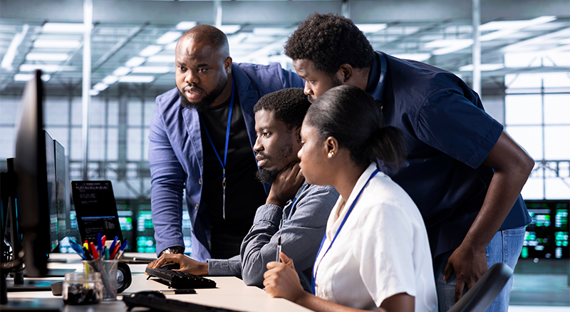 Four individuals, three men and one woman, focused on their work at computers in a collaborative office setting