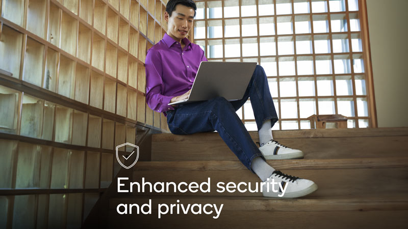 An employee sitting on steps working on laptop with text displaying 'enhanced security and privacy'