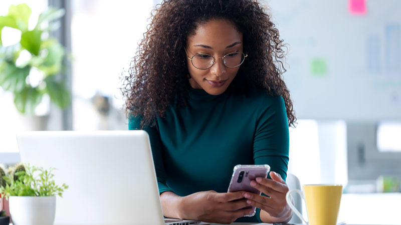 a woman using her smart phone besides her laptop