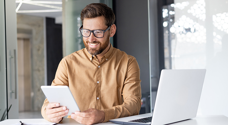 An individual smiling and working on their devices in an office.