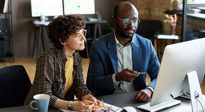 Female employee looking at desktop coputer alongside male employee