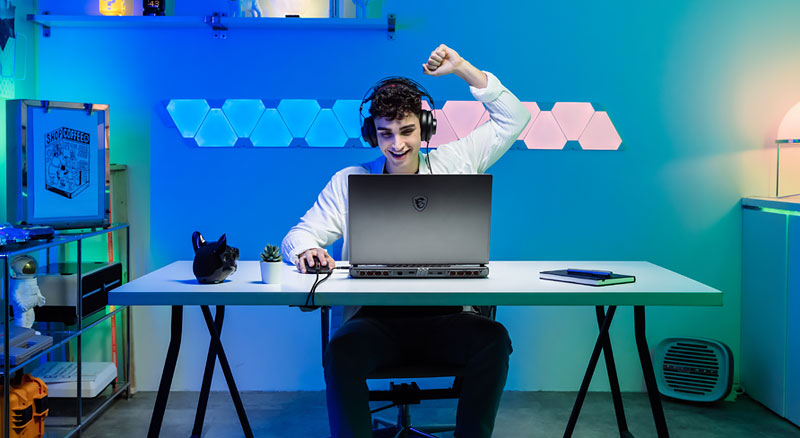 Smiling man raises his fist in celebration while gaming on his laptop