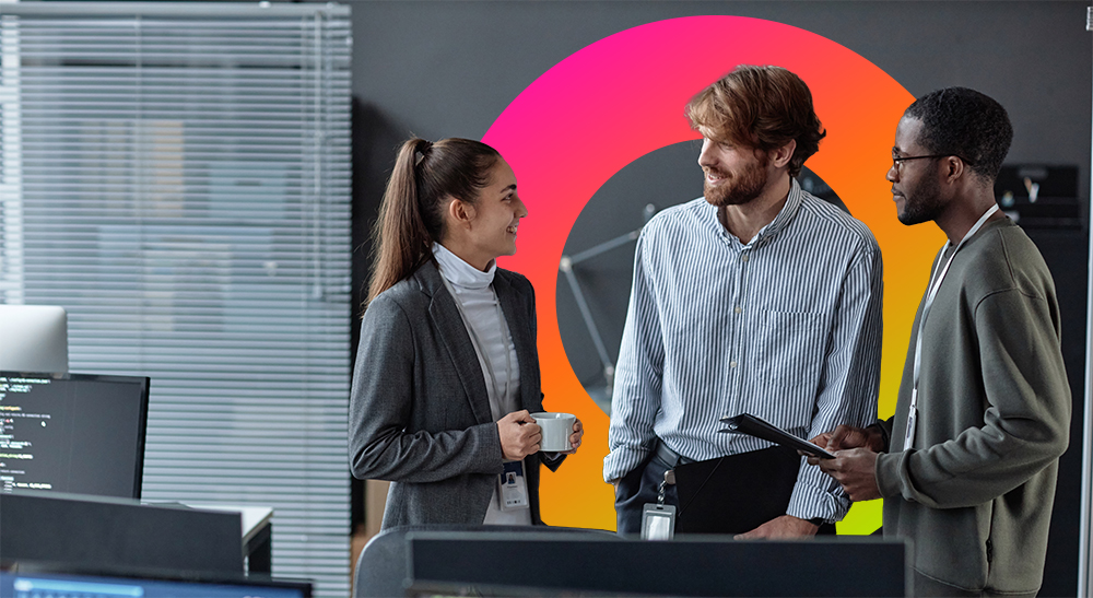 Three employees have a discussion standing behind a desk