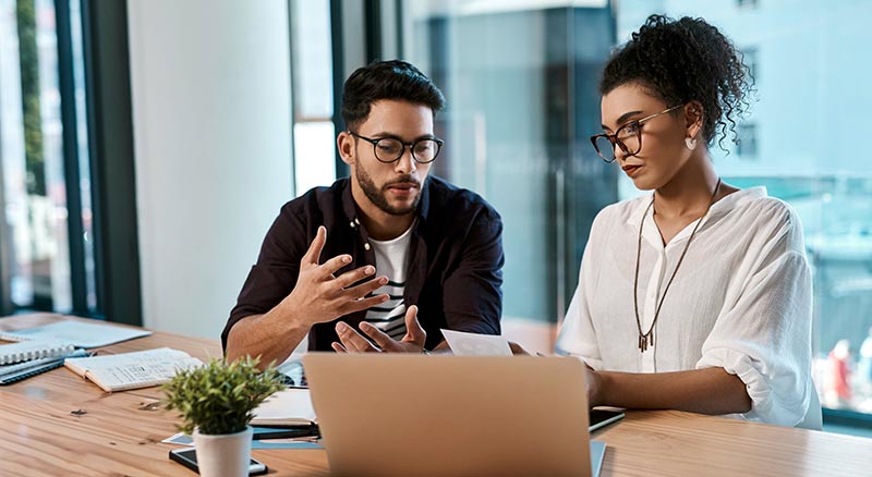 Two employees discuss information behind a laptop
