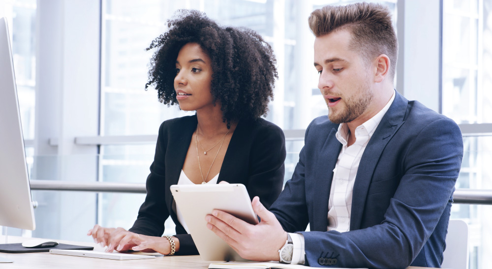 Two business professionals seated at a desk, focused on a computer screen together