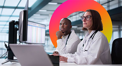 Two medical professionals using a computer with multiple monitors