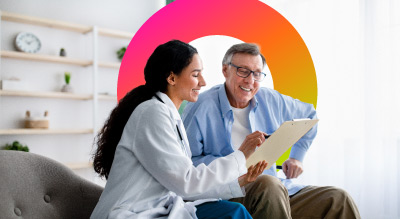 a healthcare professional and another individual engaged in a discussion over a document in a well-lit room with a grey sofa 