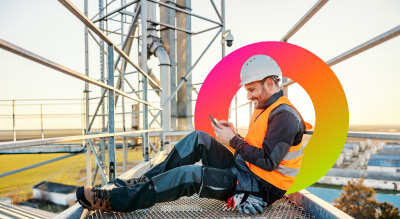 A worker in safety gear, seated on a high platform amidst industrial structures, reviewing documents