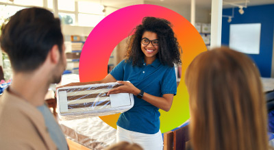 A store employee in a blue polo shirt is presenting a striped fabric sample to customers