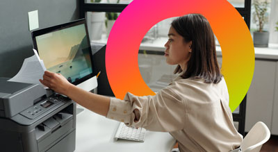 A woman in an office is using a printer next to a computer
