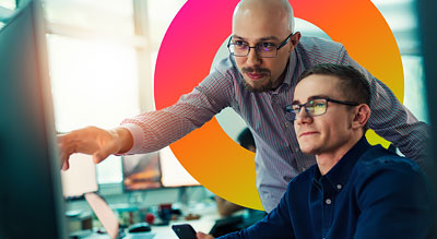 Two people in an office setting, one pointing at the computer monitor and the other looking at it