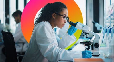 A person in a lab coat and gloves is using a microscope in a laboratory